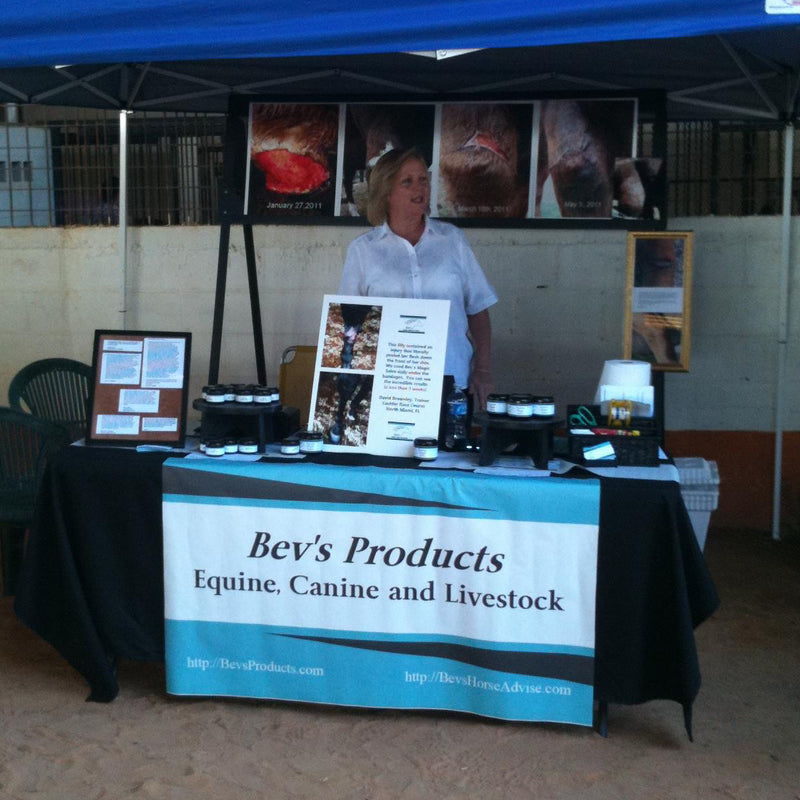 Person standing behind a table with 'Bev's Products' banner under a blue tent.